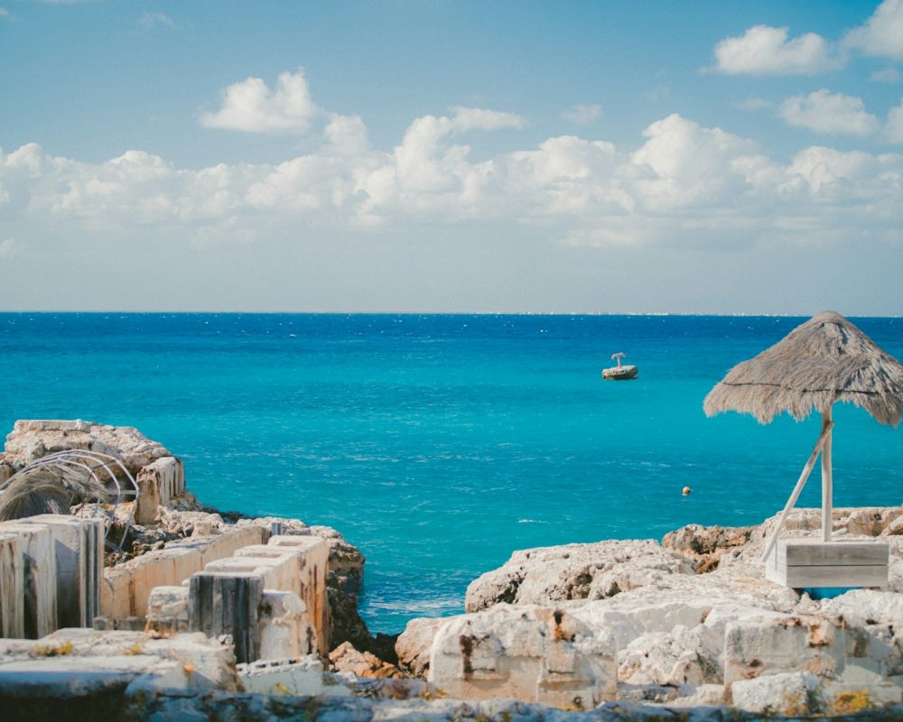thatch parasol near ruins on island and sea at the distance during day